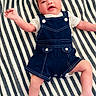 Michaela Rayne is registered to the contest to win money with this photo: arms, baby, blanket, child, close_up, cute, denim, face, fashion, happy, indoor, infant, legs, lying_down, overalls, photography, portrait, shirt, smiling, striped_blanket