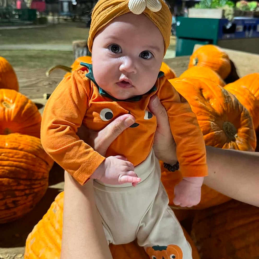 Michaela Rayne is registered to the contest to win money with this photo: baby, child, pumpkin, halloween, costume, orange, headband, flower, infant, outdoor, night, portrait, cute, wide_eyed, being_held, arms, fall, autumn, farm, festive