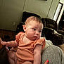 Eliza is registered to the contest to win money with this photo: baby, infant, child, person, living_room, furniture, armchair, couch, orange_clothing, skin, hand, nail_polish, indoor, floor, portrait, cute, sitting, curious, soft_light, casual