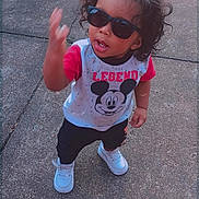 Kamran is registered to the contest to win money with this photo: toddler, child, sunglasses, mickey_mouse, legend, shirt, white_shoes, sidewalk, concrete, curly_hair, standing, casual_clothing, outdoor, person, young_child, fashion, playful, cute, expression, hand_gesture