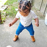 Kamran is registered to the contest to win money with this photo: toddler, child, outdoor, standing, braided_hair, white_shirt, blue_pants, boots, concrete, grass, brick_wall, sign, twelve_months, baby, young_child, casual_clothing, daylight, portrait, person, looking_down