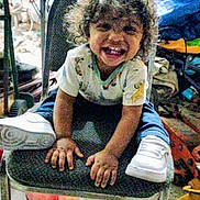 Kamran joined the competition — help win amazing prizes! candid, casual_clothing, chair, child, cluttered_background, curly_hair, expression, footwear, hands, happy, indoor, joy, person, playful, seat, sitting, smile, toddler, white_shoes, young_child