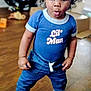 toddler, child, curly_hair, blue_shirt, denim_pants, white_sneakers, wooden_floor, indoor, standing, expression, cute, casual_clothing, person, playroom, car_seat, toy, home, portrait, young_child