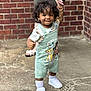 child, toddler, curly_hair, overalls, hakuna_matata, white_sneakers, socks, outdoor, brick_wall, concrete, person, hand_holding, smile, cute, fashion, baby, walking, support, footwear, casual