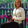 woman, dog, pet, purple_harness, tulips, flowers, fence, outdoor, portrait, smile, sitting, casual_clothing, shoulder_bag, nature, greenery, spring, small_dog, leash, happy, background