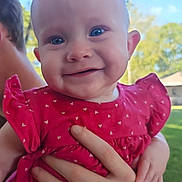 Janie is registered to the contest to win money with this photo: baby, child, smiling, blue_eyes, red_dress, heart_pattern, hand, outdoor, nature, tree, sky, person, portrait, cute, infant, holding, happy, face, skin, young
