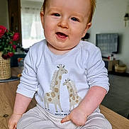 Alexis participe au concours pour gagner de l'argent avec cette photo : baby, barefoot, child, cozy, flowers, furniture, giraffe_print, happy, indoor, infant, living_room, long_sleeves, natural_light, pants, portrait, sitting, smiling, vase, white_shirt, wooden_table
