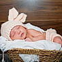 baby, sleeping, basket, knitted_hat, bunny_ears, white_blanket, wooden_background, infant, cute, cozy, newborn, soft_fabric, resting, child, portrait, indoors, wearing_clothes, peaceful, headwear, small