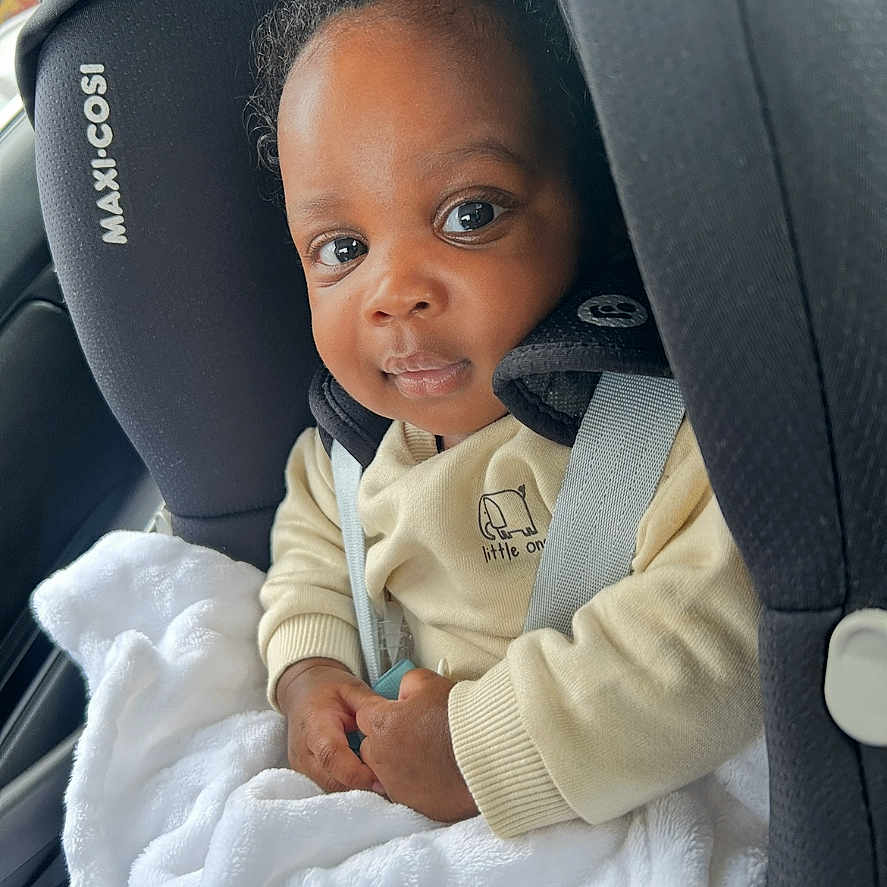 Noah is registered to the contest to win money with this photo: baby, blanket, car, car_seat, child, clothing, curly_hair, cute, face, hands, indoor, infant, looking_at_camera, maxi_cosi, person, portrait, safety, seatbelt, smiling, young_child