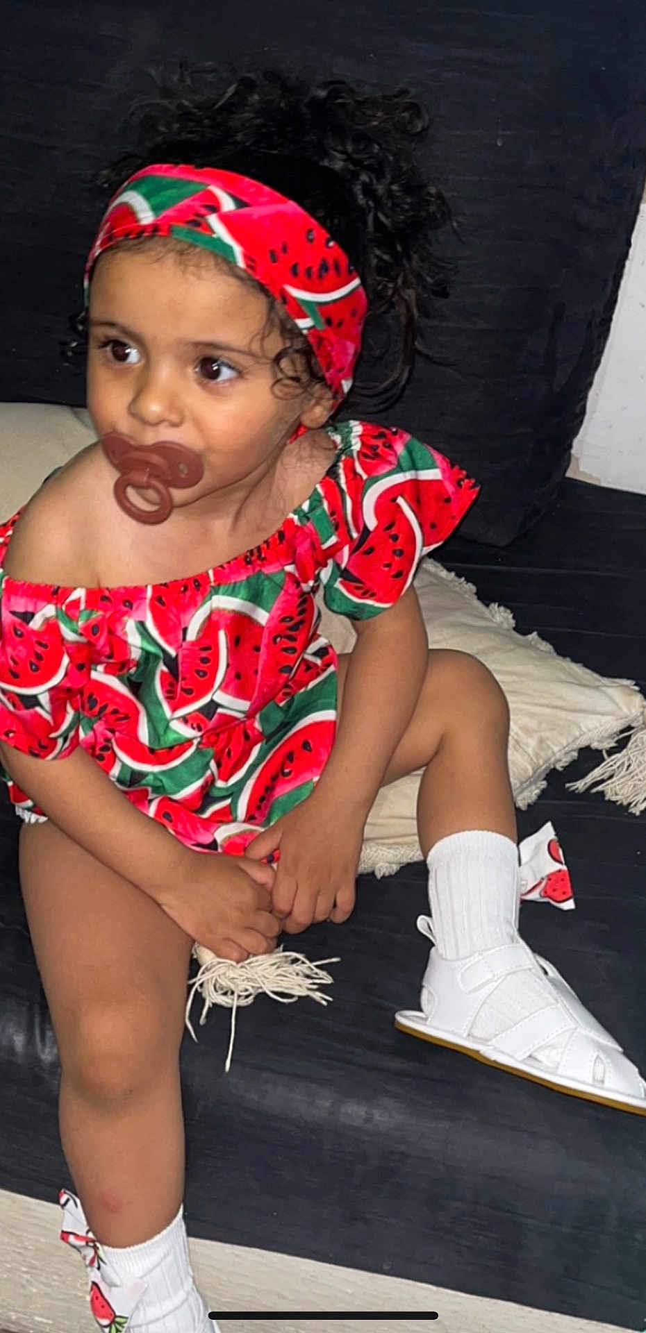 Myra participe au concours pour gagner de l'argent avec cette photo : toddler, child, pacifier, watermelon_pattern, headband, curly_hair, white_socks, white_sandals, couch, pillow, indoor, clothing, sitting, cute, small_child, person, fashion, accessory, colorful, portrait