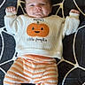 Dante is registered to the contest to win money with this photo: baby, child, infant, smiling, portrait, lying_down, spiderweb, halloween, pumpkin, onesie, striped_clothing, socks, blanket, bed, indoor, cute, happy, face, fists, seasonal_decor