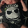 Dante is registered to the contest to win money with this photo: newborn, baby, child, infant, sleepy, lying_down, portrait, face, person, black_clothing, graphic_shirt, cartoon, skull_design, striped_socks, blanket, indoor, close_up, relaxed, patterned_background, photograph