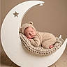 newborn, baby, sleeping, infant, portrait, moon_cradle, hammock, knitted_blanket, bear_hat, beige, cozy, indoor, wooden_floor, studio_photography, peaceful, curled_up, cute, nursery, soft_lighting, cradle