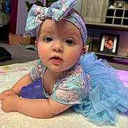 Rowan is registered to the contest to win money with this photo: baby, infant, blue_outfit, headband, bow, toy, indoor, carpet, plant, furniture, picture_frame, curtains, face, eyes, expression, toddler, child, person, cute, soft_lighting