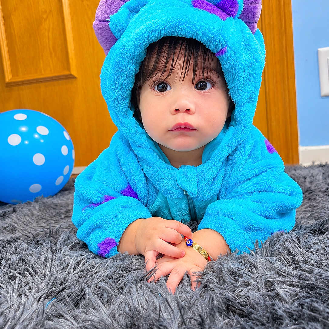 Ian Gael joined the competition — help win amazing prizes! baby, balloon, blue, bracelet, child, close_up, costume, cute, hands, home, hoodie, indoor, large_eyes, portrait, purple, rug, serious_expression, sitting, toddler, wooden_door