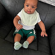 Zymeir joined the competition — help win amazing prizes! baby, child, infant, sitting, bib, green_shorts, socks, black_couch, leather, curious, portrait, indoors, person, cute, young, small, looking, comfortable, clothing, expression