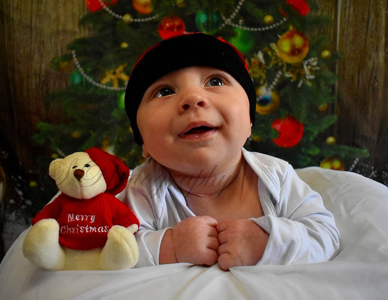 Brandon is registered to the contest to win money with this photo: baby, baby_toddler_clothing, child, christmas, comfort, event, fun, gesture, happy, headwear, holiday, nose, ornament, person, plant, room, sitting, sleeve, smile, teddy_bear