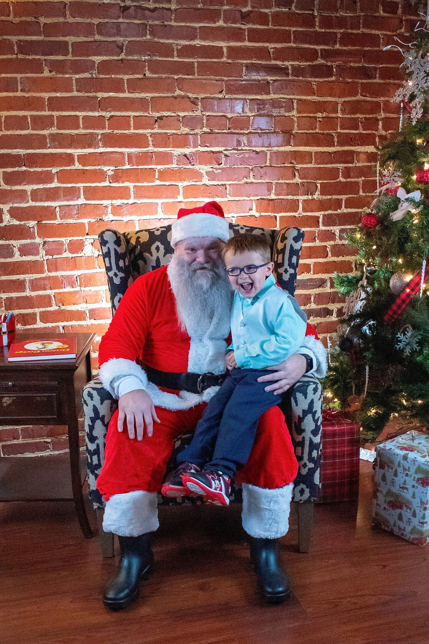 James is registered to the contest to win money with this photo: beard, brick, brickwork, christmas, christmas_tree, costume_hat, event, fun, fur, happy, hat, headwear, holiday, lap, person, plant, santa_claus, sitting, smile, standing