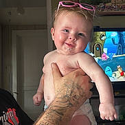 Anslee joined the competition — help win amazing prizes! baby, child, tattoo, hand, diaper, glasses, pink_sunglasses, smile, drool, hair, indoor, television, cartoon, person, skin, arm, holding, funny_hair, expression, room