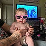 Anslee joined the competition — help win amazing prizes! baby, pink_sunglasses, tattooed_hand, diaper, indoor, television, cartoon, person, child, hair, furniture, living_room, casual, clothing, skin, hand, seated, expression, cute, home