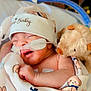 newborn, baby, hospital, medical_tubes, blanket, teddy_bear, hat, sleeping, infant, cute, child, person, healthcare, soft_toy, bed, swaddled, closeup, peaceful, resting, childcare
