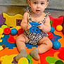 baby, child, toy, playmat, ball, colorful, indoor, sitting, cute, infant, puzzle_mat, sock, clothing, face, hands, person, hair_bow, plastic_ball, floor, playtime