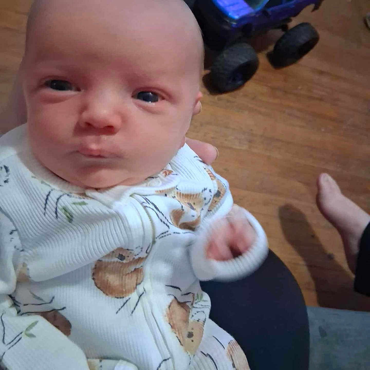 Aron is registered to the contest to win money with this photo: baby, baby_clothes, child, closeup, clothing, couch, cute, flooring, foot, furniture, hand, human, indoor, infant, onesie, person, plush_toy, portrait, toy_truck, wooden_floor