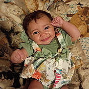 O'Dyssey joined the competition — help win amazing prizes! baby, smile, child, green_clothing, floral_dress, blanket, cat_pattern, cute, happy, portrait, infant, indoors, closeup, playful, face, skin, hand, lying_down, colorful, fabric