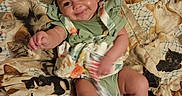 O'Dyssey is registered to the contest to win money with this photo: baby, infant, child, smiling, green_clothing, blanket, cat_pattern, illustration, fabric, lying_down, indoor, cute, playful, portrait, person, baby_shoes, colorful, happy, soft_lighting, bedroom