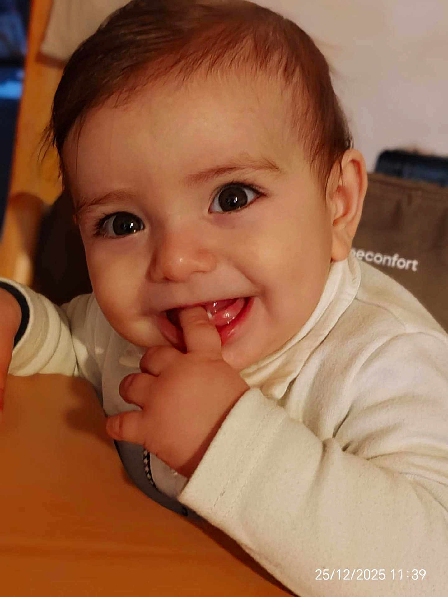 Isaac a rejoint le concours — aidez-le/la à gagner de superbes lots ! baby, child, face, fingers, smile, eyes, hand, white_clothing, high_chair, indoor, portrait, cute, infant, young_child, person, closeup, happy, chewing, table, cozy