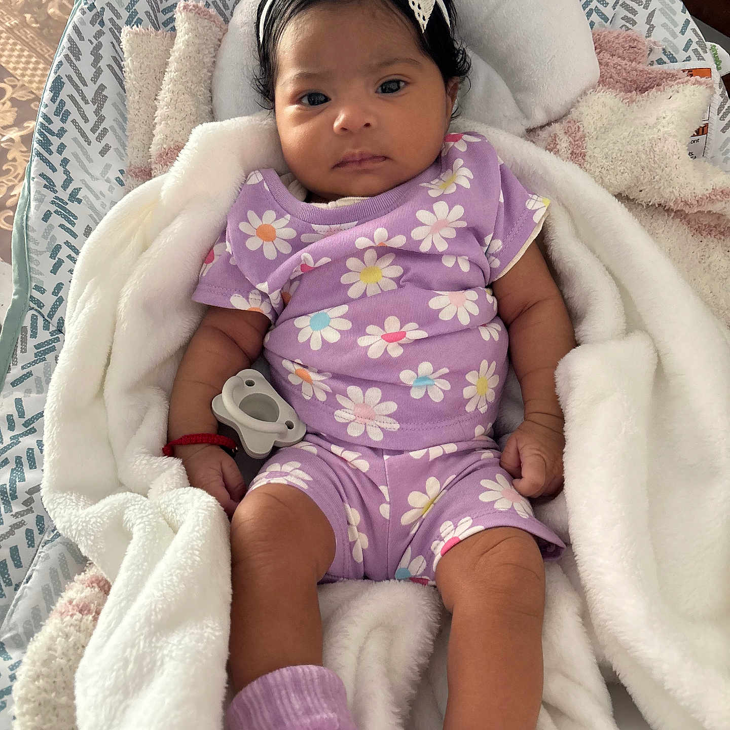 Celina is registered to the contest to win money with this photo: baby, blanket, bow, child, cozy, cute, daisy_pattern, headband, indoor, infant, newborn, pacifier, person, portrait, purple_clothing, relaxed, resting, sleepwear, socks, soft_texture