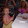 children, toddler, girl, kids, eating, food, snack, birthday_party, table, messy_table, purple_cup, hair_bow, curly_hair, dress, camouflage, glasses, indoor, restaurant, seated, portrait