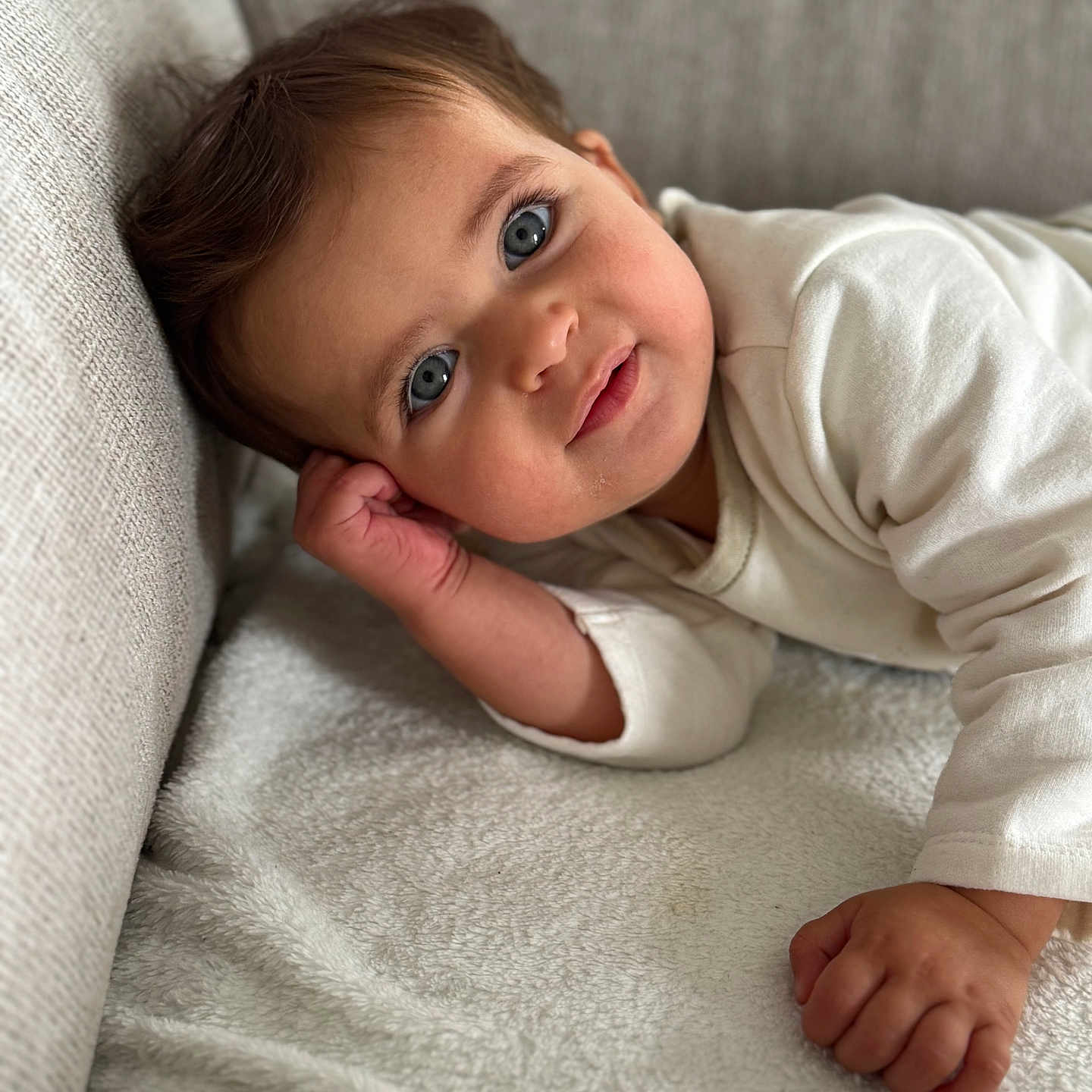 Chamss a rejoint le concours — aidez-le/la à gagner de superbes lots ! baby, blanket, blue_eyes, child, closeup, couch, cozy, curious, face, hand, head, indoor, infant, person, portrait, relaxed, skin, smile, soft_texture, white_clothing
