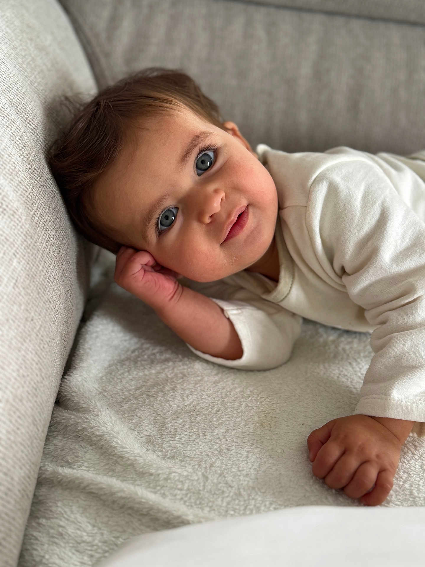 Chamss a rejoint le concours — aidez-le/la à gagner de superbes lots ! baby, blanket, blue_eyes, child, closeup, couch, cozy, curious, face, hand, head, indoor, infant, person, portrait, relaxed, skin, smile, soft_texture, white_clothing