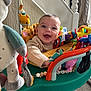 baby, smiling, child, toys, activity_center, indoor, happy, face, clothing, home, carpet, furniture, play, colorful, cute, person, sweater, expression, infant, seat