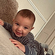 Ollie joined the competition — help win amazing prizes! baby, smiling, striped_clothing, infant, lying_down, indoor, pillow, happy, person, toddler, face, hands, feet, cozy, wall, door, floor, candid, child, cute
