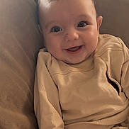 Ollie joined the competition — help win amazing prizes! baby, beige_clothing, casual_clothing, child, closeup, couch, cozy, cute, face, happy, human, indoors, infant, pillow, portrait, relaxed, sitting, smiling, soft_furniture, young_child