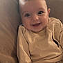 baby, smiling, child, infant, couch, pillow, beige_clothing, happy, indoors, portrait, cute, sitting, face, young_child, soft_furniture, cozy, human, casual_clothing, relaxed, closeup