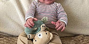 Julien participe au concours pour gagner de l'argent avec cette photo : baby, beige_pants, blanket, casual_clothing, child, cozy, cute, drool, happy, indoor, infant, person, plush_toy, portrait, seated, smiling, socks, soft_toy, striped_shirt, texture