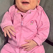 Natalie is registered to the contest to win money with this photo: baby, pink_clothing, smiling, happy, infant, couch, gray_furniture, indoor, portrait, child, one_person, seated, cute, cozy, relaxed, face, hands, footed_pajamas, zipper, flower_patch