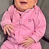baby, pink_clothing, smiling, happy, infant, couch, gray_furniture, indoor, portrait, child, one_person, seated, cute, cozy, relaxed, face, hands, footed_pajamas, zipper, flower_patch