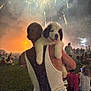 person, puppy, dog, fireworks, night, outdoor, crowd, grass, celebration, festival, smoke, light, shoulder, tank_top, happy, pet, event, relaxation, fun, companionship