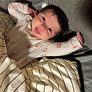 Selah is registered to the contest to win money with this photo: baby, child, face, smile, eyes, blanket, striped_blanket, clothing, onesie, bed, pillow, happy, infant, lying_down, cute, indoors, person, skin, hair, stretching