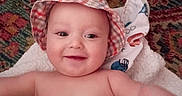 O'Ryen is registered to the contest to win money with this photo: baby, child, hat, smile, blanket, bottle, carpet, pattern, indoor, happy, cute, infant, person, toddler, skin, expression, lying_down, baby_bottle, headwear, cheerful