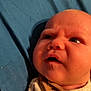Ambrose is registered to the contest to win money with this photo: baby, infant, face, expression, curious, clothing, bib, blue_background, closeup, skin, head, newborn, person, child, young, indoors, portrait, sleepwear, soft_light, laying_down