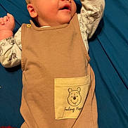 Ambrose is registered to the contest to win money with this photo: baby, infant, child, smiling, clothing, onesie, pocket, bear, blue_blanket, happy, cute, lying_down, raised_arm, face, skin, head, hand, bed, fabric, comfort