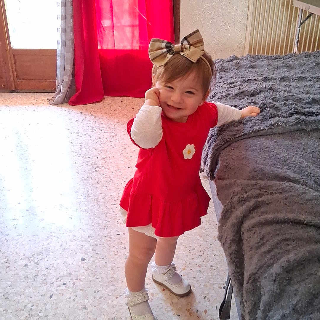 Kamelya a rejoint le concours — aidez-le/la à gagner de superbes lots ! toddler, child, red_dress, bow, headband, smile, indoor, blanket, bed, curtain, floor, radiator, window, door, white_shoes, happy, pose, person, home, cozy