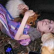 Stella is registered to the contest to win money with this photo: blanket, brown, carpet, casual, child, comfort, couch, cozy, dog, face, fur, home, hugging, indoor, pet, purple, relaxing, remote_control, smartphone, white
