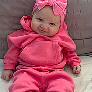 Ivy is registered to the contest to win money with this photo: baby, infant, pink_clothing, headband, bow, hoodie, pants, sitting, cute, smiling, pillow, soft_fabric, indoors, child, portrait, young_child, cozy, person, sock, comfortable