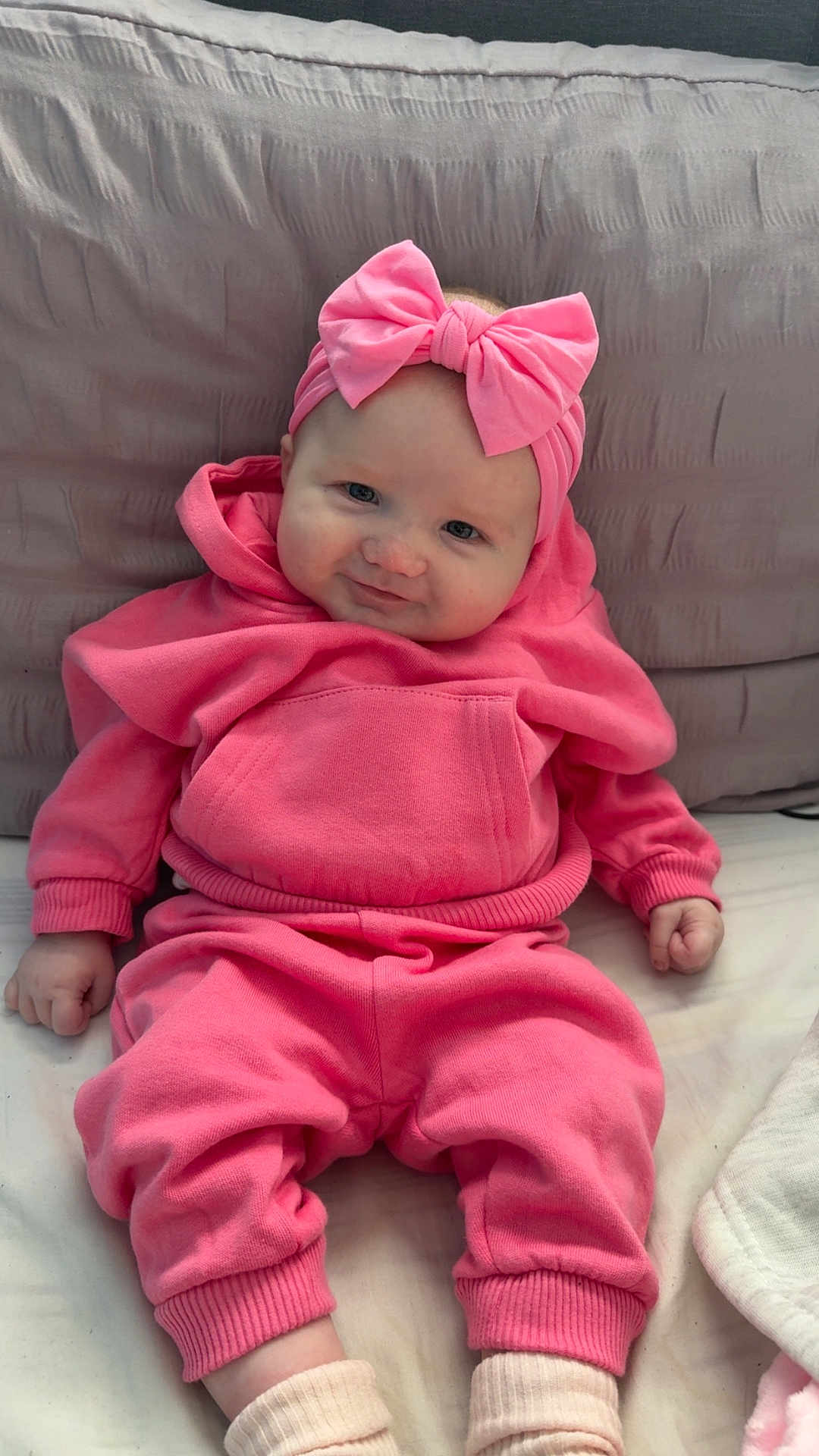 Ivy is registered to the contest to win money with this photo: baby, infant, pink_clothing, headband, bow, hoodie, pants, sitting, cute, smiling, pillow, soft_fabric, indoors, child, portrait, young_child, cozy, person, sock, comfortable